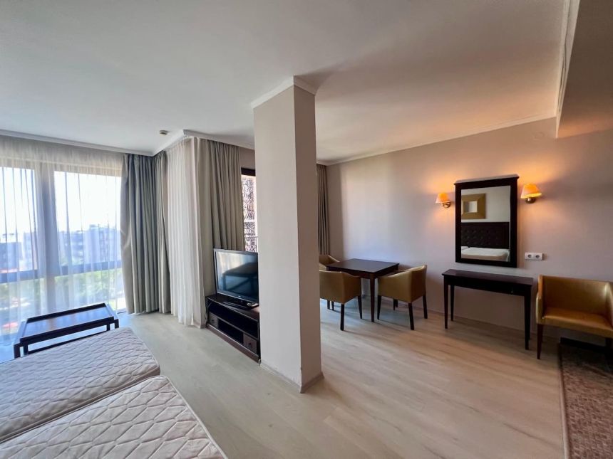 Планировка студии Barcelo Royal Beach — спальная зона, телевизор и обеденный стол с креслами